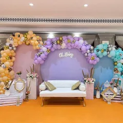 This large-scale baby shower decoration shows how we can transform a venue space. The setup includes three distinct pastel-colored backdrops with balloon arches and a central sofa, providing ample, beautiful seating for the guests of honor.