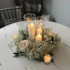 An elegant and classic centerpiece design with pillar candles in glass vases, surrounded by a wreath of baby's breath and a single pink rose.