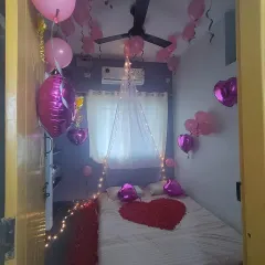 Another view of a romantic room decoration, showing the arrangement of pink balloons, heart-shaped foil balloons, and a bed adorned with rose petals.