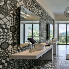 This bathroom in a Khandala villa uses bold black and white patterned tiles on both the floor and the feature wall. The floating concrete vanity and large mirrors create a sense of space, while the windows offer a view of the lush green landscape.