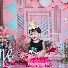 A little boy enjoys his pink-themed cakesmash, with frosting on his hands and a happy expression. The elaborate pink and blue geometric background shows the level of detail in my themed setups.