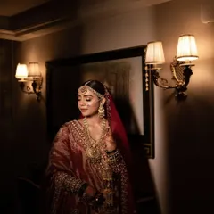 A stunning bridal portrait taken in a warmly lit hallway. The bride's intricate lehenga and jewelry are highlighted beautifully, creating an image of pure elegance.