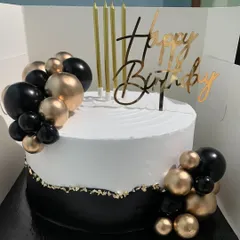 This black and gold themed cake is the definition of chic. The elegant design features a clean white top, a contrasting black base with gold leaf, and balloon-like spheres, perfect for a sophisticated birthday celebration.