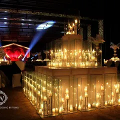 A glamorous anniversary celebration with a dramatic red and black theme. The room is filled with candlelit tables, large white feather centerpieces, and a stunning stage with a heart-shaped light installation.