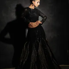 This black fusion lehenga is all about drama and texture. The skirt features unique, wave-like sculpted details, paired with a sleek, long-sleeved sequin crop top for a look that is both edgy and sophisticated.