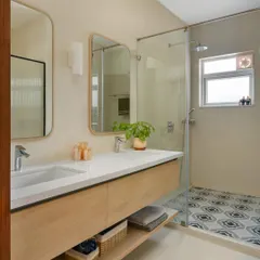 This bathroom in 'House of Kismish' features a floating wooden vanity with dual sinks and beautiful patterned floor tiles. The design is clean, modern, and has a touch of Mediterranean charm.