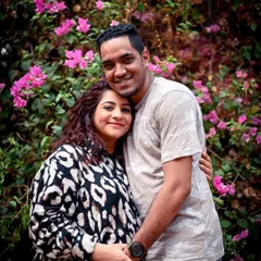 An expecting couple shares a warm embrace in a lovely garden setting. This portrait is natural and relaxed, showcasing their connection amidst the vibrant colors of the flowers.