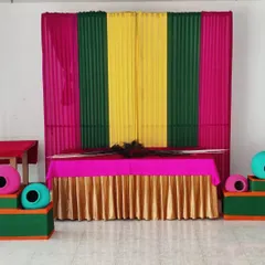 A clear, straight-on view of the completed Janamashtmi backdrop and table. The peacock feathers are placed on the table, ready for the final idol placement.