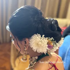 A side view of a voluminous and textured low bun, adorned with large white chrysanthemums and baby's breath. This updo is perfect for a bride who wants a romantic and floral-heavy look.