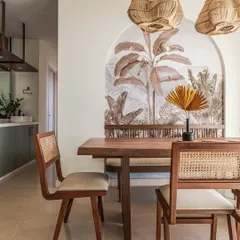 The dining area is a perfect blend of natural textures and traditional craftsmanship. A live-edge wooden table is paired with cane-backed chairs, set against a stunning tropical wallpaper mural that acts as a focal point within an arched niche.