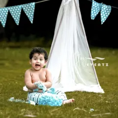 An outdoor cake smash for a one-year-old boy. This session captures the pure joy and excitement of a first birthday, with the baby happily digging into a blue rosette cake in a park setting.