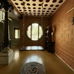 A quiet corner for reflection. This space combines a traditional indoor swing with a modern filler slab ceiling made of clay pots, reducing concrete usage while creating a unique visual texture. The large circular window frames the world outside, making nature a part of the home's interior life.