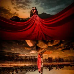For pre-wedding shoots, we can get truly creative. This dramatic shot uses a flowing red gown against a sunset sky, with a perfect reflection in the water below, to create a powerful and artistic image.