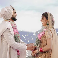 A joyful, candid moment between the couple during their varmala ceremony, with the beautiful mountain landscape visible behind them.