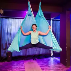 A wide-legged split supported by a vibrant blue aerial hammock. This pose demonstrates how the fabric can be used to achieve deep hip openers and stretches that might be challenging on the mat alone.
