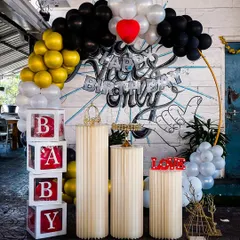 For a cool and urban vibe, we created this setup featuring a black, gold, and white balloon arch against a graffiti art wall. The arrangement includes 'BABY' blocks and fluted pedestals, blending modern decor with street art style.