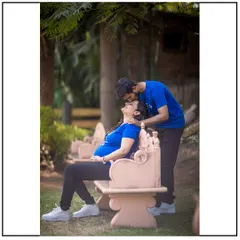 A candid and happy moment between a couple in matching blue t-shirts, enjoying a laugh on a park bench.