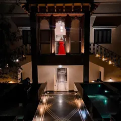 A dramatic portrait in a heritage location. The bride-to-be in a striking red dress, framed by the traditional architecture, creates a powerful and cinematic image worthy of a movie poster.