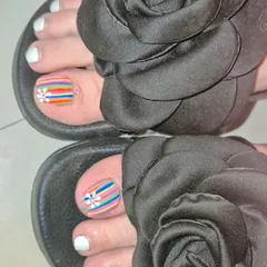 A chic pedicure with a mix of solid white polish and accent toes featuring colorful rainbow stripes and a delicate daisy.