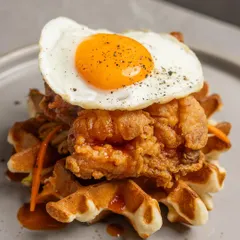 A full view of our Fried Chicken and Waffles, stacked high and topped with a perfect sunny side up egg. A true brunch centerpiece.