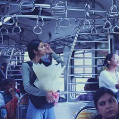 Another commuter in the Mumbai local, holding a bouquet of white flowers. This candid shot captures her standing journey, a common sight in the city's lifeline.