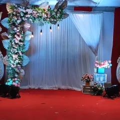 A stage setup designed for a formal ceremony or presentation. The asymmetrical floral arch, combined with simple white draping and professional lighting, creates a focal point that is both elegant and professional.