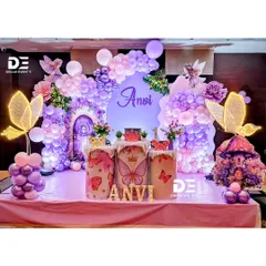 A whimsical fairy and butterfly theme for Anvi's first birthday. The decor features a magical purple door backdrop, illuminated butterfly props, and a soft, dreamy balloon arch in shades of pink and purple.