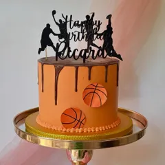 An action-packed basketball cake with a chocolate drip. The custom topper shows players in silhouette, making it a dynamic centerpiece for a birthday.