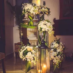 Creating a warm welcome with clusters of classic white floral arrangements and lanterns. The combination of soft candlelight and fresh flowers in tall glass vases provides a sophisticated and inviting ambiance for any gala.