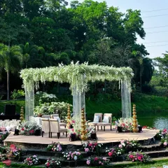 The lakeside mandap design, featuring acrylic pillars and a ceiling of hanging white flowers, offers a breathtaking view and an atmosphere of pure elegance for the wedding ceremony.
