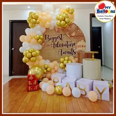 A "Biggest Adventure Awaits" themed baby shower. The travel-inspired decor includes a world map backdrop, vintage-style suitcases, and 'BABY' blocks, all in a neutral peach and gold palette.