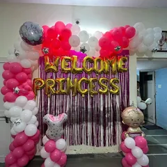 A "Welcome Princess" home decoration featuring a vibrant pink and white balloon arrangement. The backdrop is a shimmer foil curtain, complemented by foil baby character balloons and balloon columns.