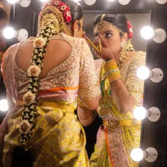 A getting-ready shot showing the back of a bridal blouse with a heart-shaped cutout. The entire blouse is covered in delicate embroidery, and the traditional braided hairstyle is adorned with flowers, completing the muhurtham look.