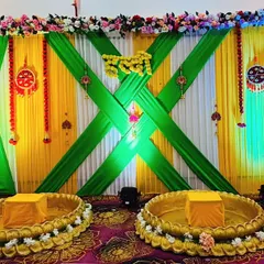 For a grander celebration, I designed this elaborate stage with crisscrossing green drapes over a yellow and white base. The two large brass urlis provide traditional seating for the couple, making it a stunning focal point.