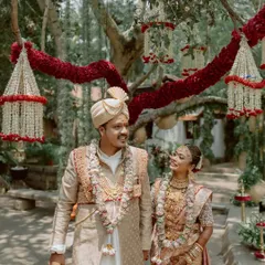 A couple walks through the gardens, framed by hanging floral decorations, a beautiful and romantic shot.