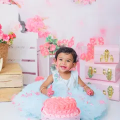 All smiles and covered in pink frosting! This happy toddler is having the best time during her cake smash session, set against a beautiful backdrop of pink flowers and vintage boxes.