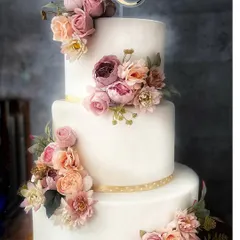 A full view of the magnificent three-tier wedding cake, adorned with a cascading arrangement of delicate, handcrafted sugar flowers.