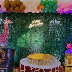 A detailed look at our jungle-themed birthday decor. A faux grass wall provides a natural backdrop for a neon sign, while animal props and themed cake stands complete the safari vibe.
