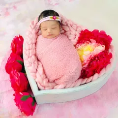 A newborn baby swaddled in pink and nestled in a heart-shaped basket surrounded by flowers. A truly lovely and artistic way to capture your new love.