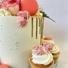 A detailed close-up of the elegant floral cake, showing the texture of the buttercream, the precise gold drip, and the delicate piping on the matching cupcakes.