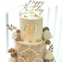 A grand two-tiered cake for a 50th birthday. The intricate gold stenciling and white roses create a look of pure luxury.