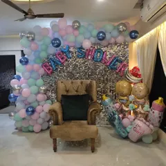 A beautiful baby shower setup for a baby girl. This design features a silver sequin wall, a pastel pink, blue, and mint balloon arch, and large foil balloons spelling 'Baby Shower' and 'It's a Girl'.