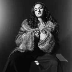 A glamorous black and white portrait. The high-contrast lighting emphasizes the texture of the faux fur coat and the model's confident expression.
