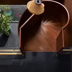 A top-down view of the blackened steel spiral staircase at the Baid Residence. The design is both a functional connector and a sculptural object, its precise geometry creating a powerful visual statement.