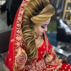 A beautiful bride ready for her ceremony. This look features a detailed, side swept hairstyle that adds volume and elegance, perfectly matching her traditional red bridal outfit and jewelry.