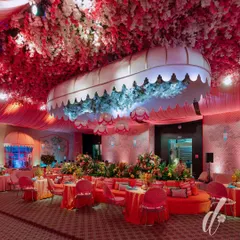 The evening look of our 'La Dolce Vita' theme, where the space was transformed with dramatic pink lighting. A custom canopy filled with blue hydrangeas became a central feature, surrounded by plush orange seating and tables set for a luxurious dinner.