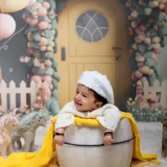 A real-life doll in a whimsical world. This creative setup, inspired by a dollhouse with a beautiful balloon arch, creates a magical and playful scene for a milestone photoshoot.