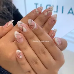 An elegant abstract design on almond-shaped nails. A sheer nude base is decorated with delicate, free-flowing brown and white lines, creating a minimalist yet artistic look.