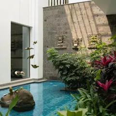 A small, intimate pool surrounded by stone walls and lush planting. The design includes traditional carved stone reliefs and brass bird sculptures, adding layers of art and culture to the water feature.
