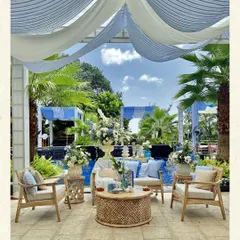 A poolside lounge setup for a daytime brunch. The airy blue and white striped drapes, natural cane furniture, and fresh floral arrangements create a relaxed, sophisticated atmosphere that is perfect for a sunlit celebration.